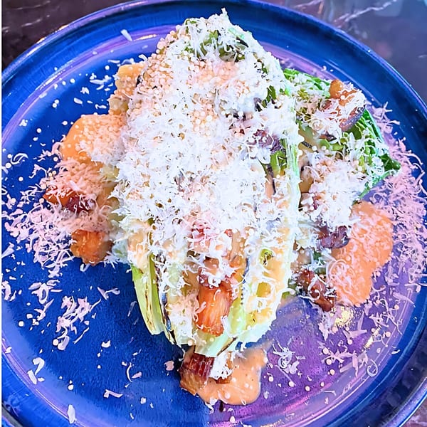 Grilled romaine lettuce with creamy dressing, crispy toppings, and grated cheese on a blue plate.