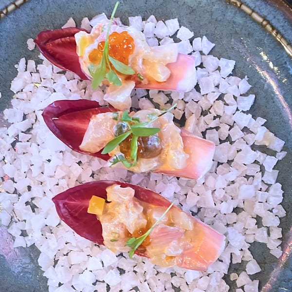 Three vibrant sushi appetizers on radicchio leaves, topped with roe and greens, served on a bed of salt.