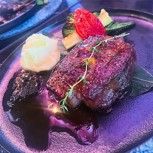 Grilled steak with mashed potatoes, dark sauce, and roasted vegetables on a black plate.